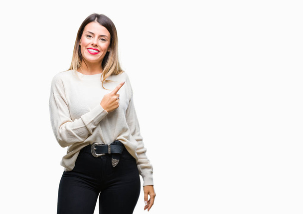Молодая красивая женщина случайный белый свитер на изолированном фоне веселый с улыбкой лица указывая рукой и пальцем в сторону со счастливым и естественным выражением лица, глядя на камеру
. - Фото, изображение