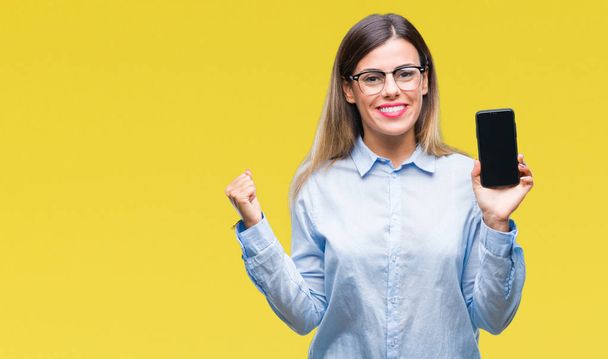 Young beautiful business woman showing blank screen of smartphone over isolated background screaming proud and celebrating victory and success very excited, cheering emotion - Photo, image