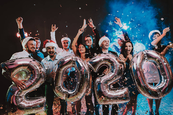 Smiling People with Baloons Celebrating New Year. Celebrating of New Year. Young Woman in Dress. Young Man in Suit. Santa Claus Cap. People with Gray Baloons. Happy New Year. People Have Fun. - Foto, imagen