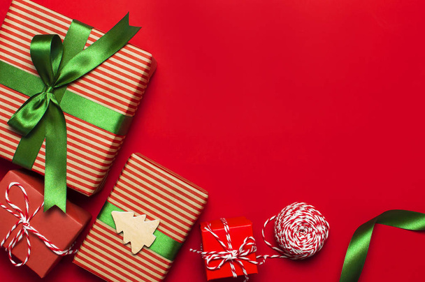 Κουτιά δώρου με κορδέλα πράσινο σε κόκκινο φόντο το top view επίπεδη θέσει. Έννοιας διακοπές, νέο έτος ή το πλαίσιο δώρο Χριστουγέννων, παρουσιάζει χριστουγεννιάτικες διακοπές. Συγχαρητήρια στο παρασκήνιο χώρο για το κείμενο. - Φωτογραφία, εικόνα