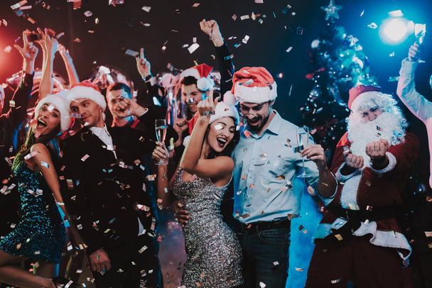 fröhliche junge Leute tanzen auf einer Silvesterparty. Weihnachtsmann. Menschen in roten Mützen. Frohes neues Jahr Konzept. Glas Champagner. Neujahrsfeiern. junge Frau in Kleid. Männer in Anzügen. - Foto, Bild