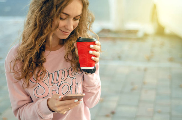 Beautiful woman in jeans and a sweatshirt with coffee smartphone mobile phone - Photo, Image