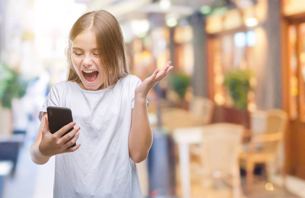 Young beautiful girl sending message texting using smarpthone over isolated background very happy and excited, winner expression celebrating victory screaming with big smile and raised hands - Photo, Image