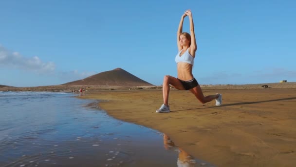 Yoga retreat and training - woman in yoga pose at beach at sunrise. Female yoga girl working out training in serene ocean landscape. SLOW MOTION STEADICAM - Footage, Video