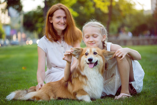 cheerful family - smiling mom and daughter and corgi fluffy  sit on the lawn - Photo, Image