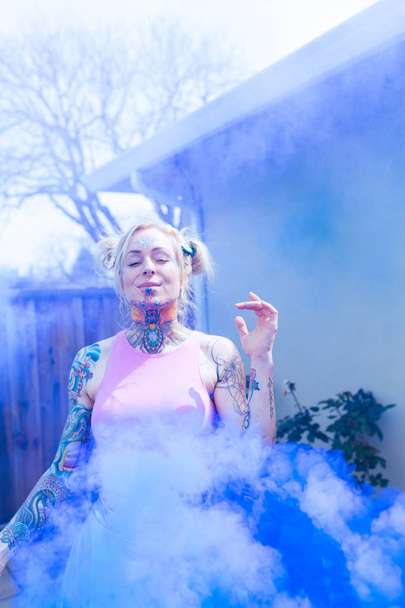 Μεγάλη πορτρέτο του Ξανθιά καυκάσιος γυναίκα με τατουάζ χρησιμοποιώντας μπλε καπνού βόμβα σε μια αστική περιοχή - Φωτογραφία, εικόνα