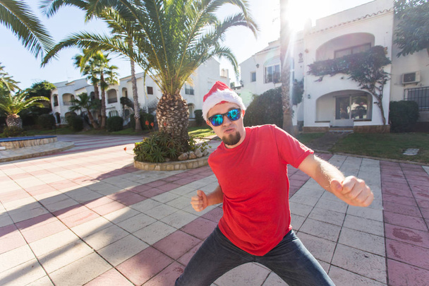 Urlaub und Menschen-Konzept - lustiger Mann mit Weihnachtsmütze tanzt draußen - Foto, Bild