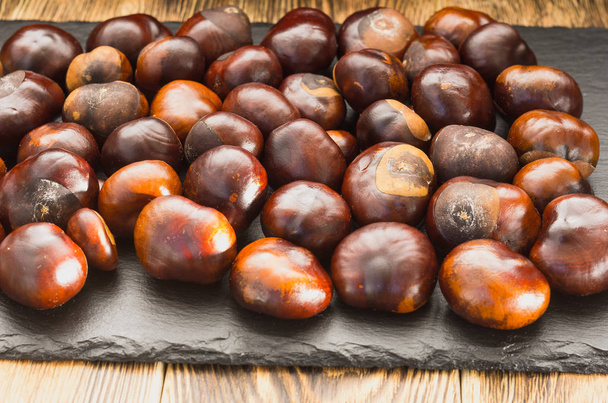 many chestnut fruits are located on a wooden table view from the side. - Photo, Image