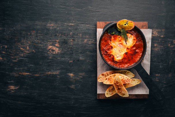 Eggs with tomatoes and toast bread in a frying pan. Shakshuka Top view. Free space for your text. On a wooden background. - Foto, imagen