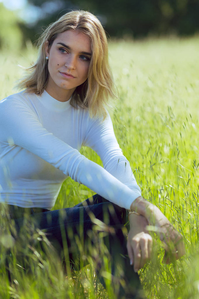 Attraente giovane bionda donna caucasica in top bianco stretto e denim posa all'esterno in erba lunga
 - Foto, immagini