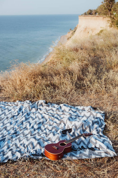 Kaş ukulele ve battaniye üzerinde kayalık sahil üzerinde gündoğumu içinde yalan güneş gözlüğü - Fotoğraf, Görsel