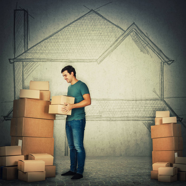 Full length portrait of young man packing stuff in boxes ready to move in another house. Home changing delivery concept over grey wall background.  - Photo, Image