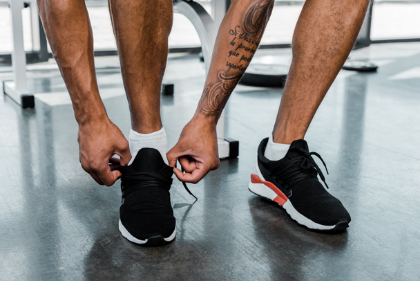 cropped shot of young sportsman tying shoelaces in gym  - Фото, изображение