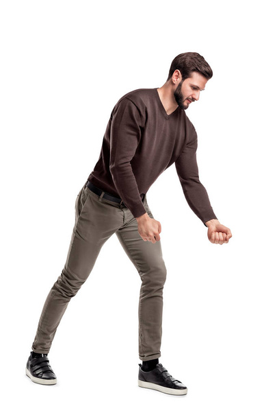 A fit bearded young man in casual clothes tries to pull an invisible rope with all his strength from low grip. - Fotoğraf, Görsel