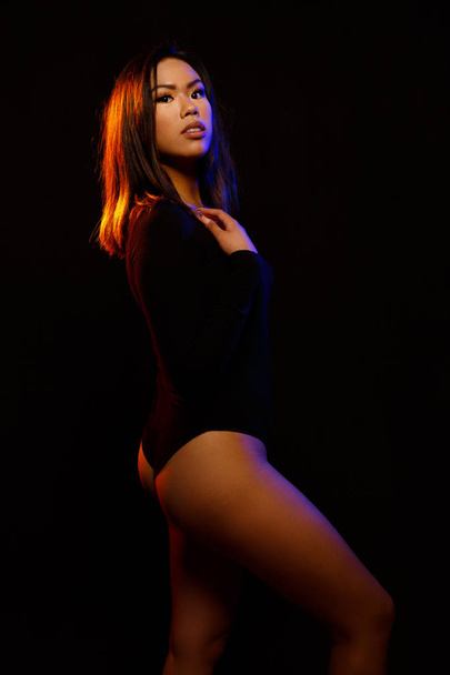 Sopii nuori aasialainen nainen musta yksiosainen ja kaulakoru aiheuttaa vastaan musta oranssi ja sininen värillinen valot
 - Valokuva, kuva