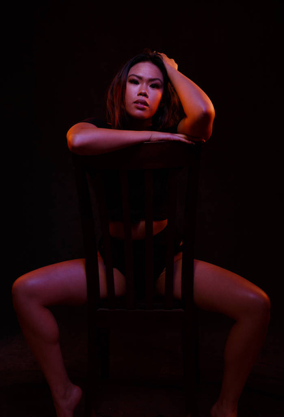 Sopii nuori aasialainen nainen musta yksiosainen aiheuttaa tuolilla alla värilliset valot
 - Valokuva, kuva