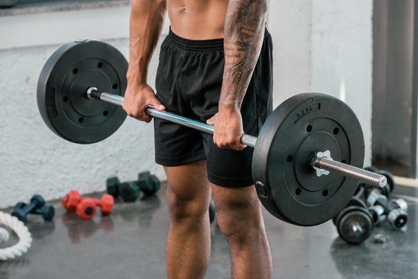 przycięty Zrzut z mięśni młody sportowiec trzymając sztangę w siłowni - Zdjęcie, obraz