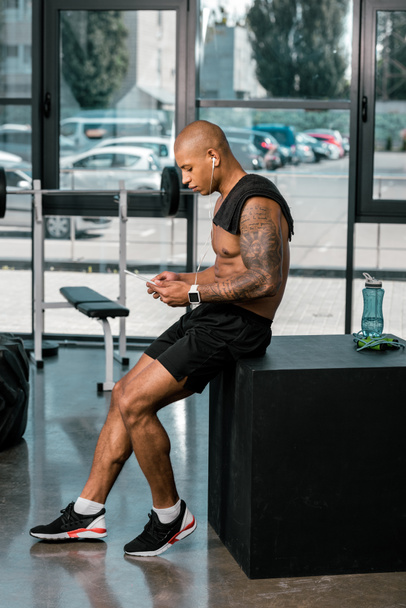 boční pohled na svalové mladého Tetovaný africké americké sportovce pomocí digitálních tabletu v tělocvičně - Fotografie, Obrázek