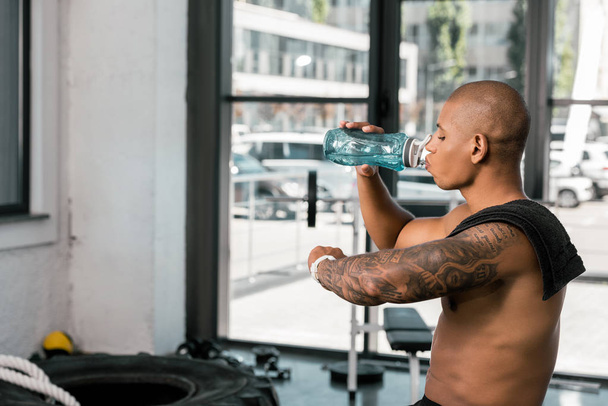 side view of young muscular man drinking water and checking smartwacth in gym - Photo, Image