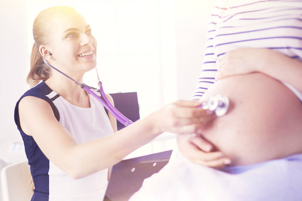 Mladá žena lékař se stetoskopem mluvit s těhotnou ženou v nemocnici. - Fotografie, Obrázek
