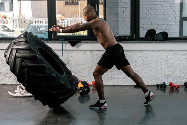 vista laterale dell'uomo muscoloso senza maglietta che si allena con lo pneumatico in palestra
  - Foto, immagini