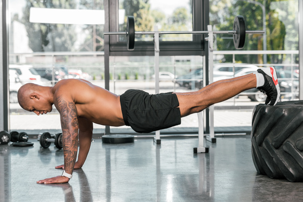 oldalnézetből izmos afrikai amerikai férfi során push ups edzőteremben gumiabroncs  - Fotó, kép