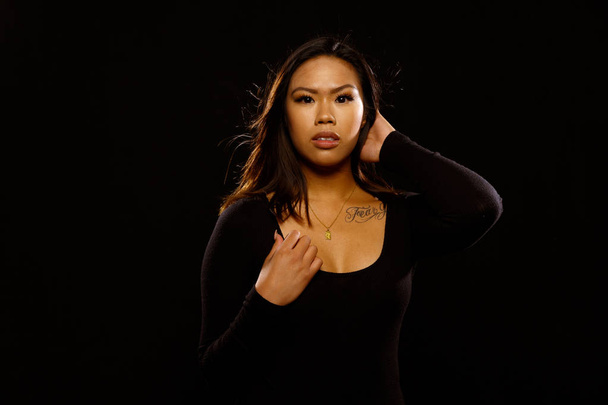 Sopii nuori aasialainen nainen musta yksiosainen ja kaulakoru aiheuttaa vastaan musta tausta
 - Valokuva, kuva