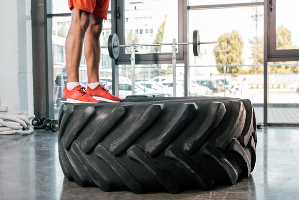 cropped image of sportsman in sneakers standing on tire at gym - Valokuva, kuva