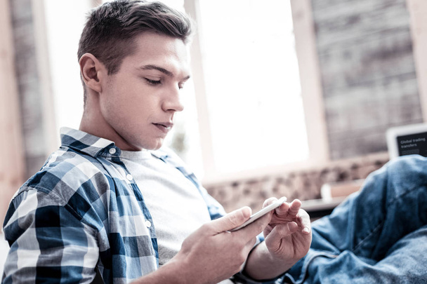 Serious young man wearing casual clothes and looking at the screen of his device - Foto, immagini