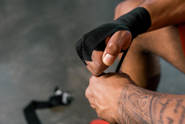 bijgesneden afbeelding van getatoeëerd sportman hand inwikkeling in boksen pleister op sportschool - Foto, afbeelding