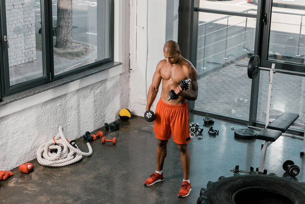 Hochwinkelaufnahme muskulöser, hemdloser afrikanisch-amerikanischer Sportler, der im Fitnessstudio mit Kurzhanteln trainiert - Foto, Bild