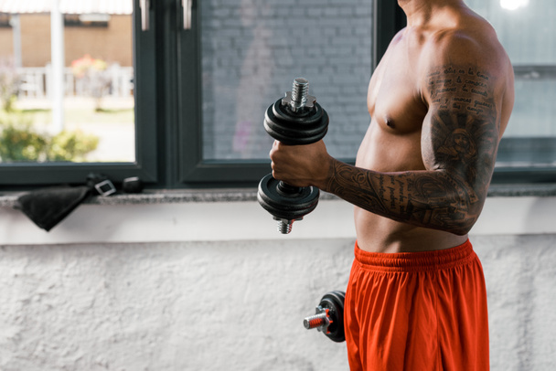 cropped image of muscular shirtless african american sportsman exercising with dumbbells at gym - Fotografie, Obrázek