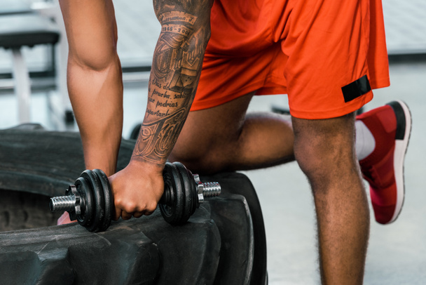imagen recortada de deportista afroamericano tatuado haciendo ejercicio con mancuerna en el gimnasio
 - Foto, Imagen