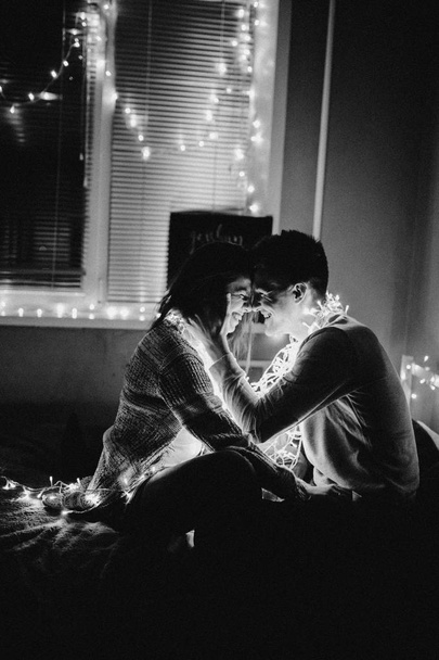 Casal amoroso abraçar uns aos outros na cama envolto em guirlanda no quarto. Foto em preto e branco com filtro de ruído
 - Foto, Imagem