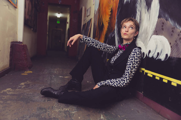Queer woman in button up shirt and tie poses in a colorful hallway - Фото, изображение