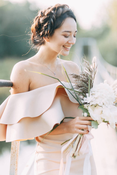 Beautiful bride in front of wedding arch with flowers and decor. Bouquet in the hands and details. The girl is happy, smiling and dancing. Dream wedding dress in modern style - Foto, Bild