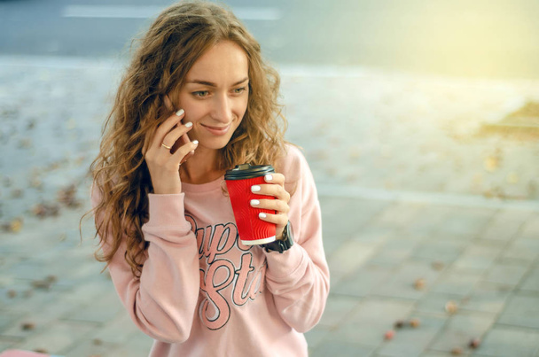 Beautiful woman in jeans and a sweatshirt with coffee smartphone mobile phone - Photo, image