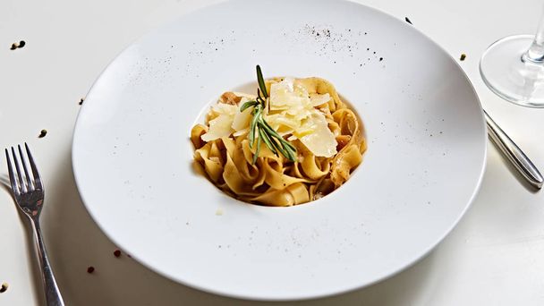 Placa de pasta italiana de primer plano con queso parmesano rallado y hoja de albahaca
 - Foto, Imagen
