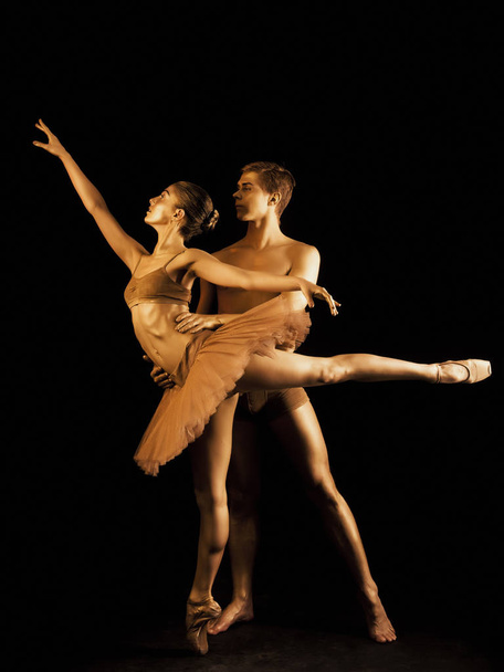 Professional, emotional ballet dancers on dark scene performed by sexual couple with golden body art.Shining gold skin.Pair depicts love and passion on stage - Foto, afbeelding