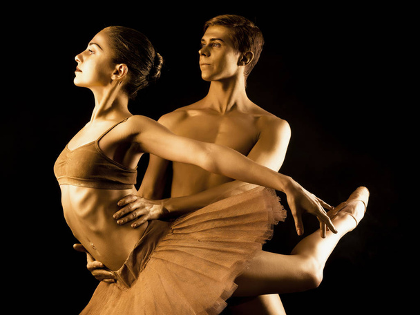 Professional, emotional ballet dancers on dark scene performed by sexual couple with golden body art.Shining gold skin.Pair depicts love and passion on stage - Photo, Image