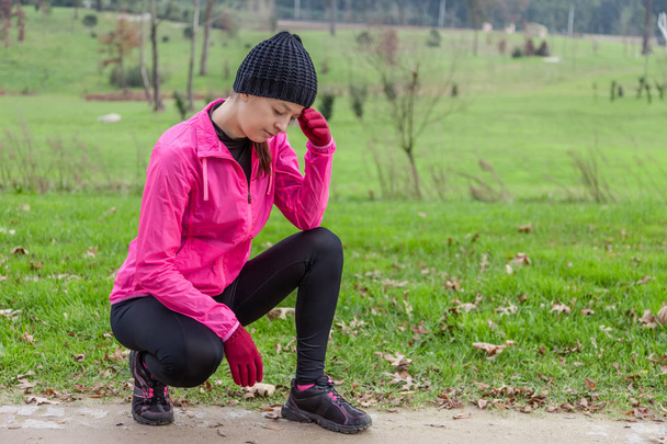Νεαρός αθλητής γυναίκα αίσθημα ζαλάδας ή με πονοκέφαλο σε μια κρύα χειμερινή ημέρα στο κομμάτι του αστικού πάρκου. - Φωτογραφία, εικόνα