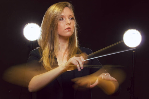 Jeune femme caucasienne chef d'orchestre gestes avec bâton et laisse des pistes de lumière
 - Photo, image