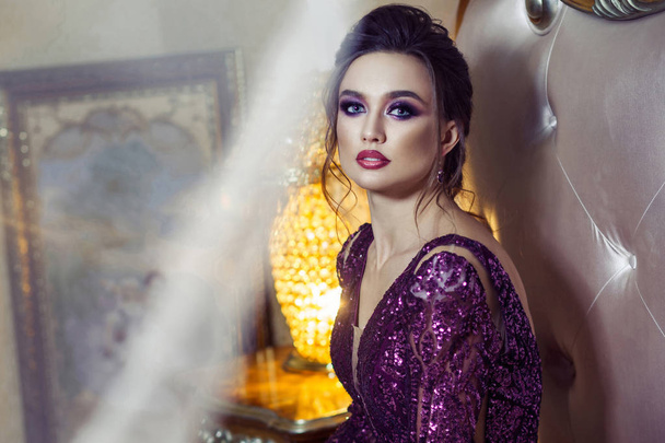 attractive woman in evening purple shiny dress sitting on bed  - Foto, Imagen