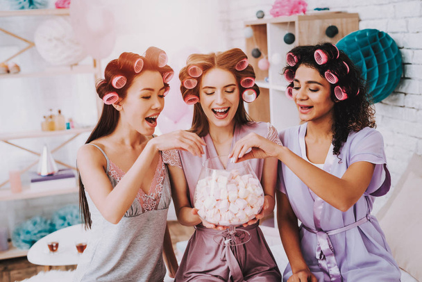 Girls with Marshmallows. Celebrating Women's Day. Emotional Women. Cheerful Women. Beautiful Girl. Girls with Hair Curlers. Marshmellow in Hands. International Women with Hair Curlers. White Interior. - Fotó, kép