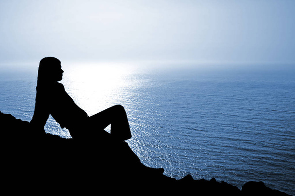 Silueta de mujer sentada contra el paisaje marino azul profundo
 - Foto, Imagen