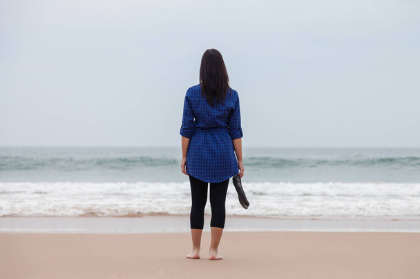 Lonely and depressed woman standing in front of the sea in a deserted beach on an Autumn day. - Foto, Imagem