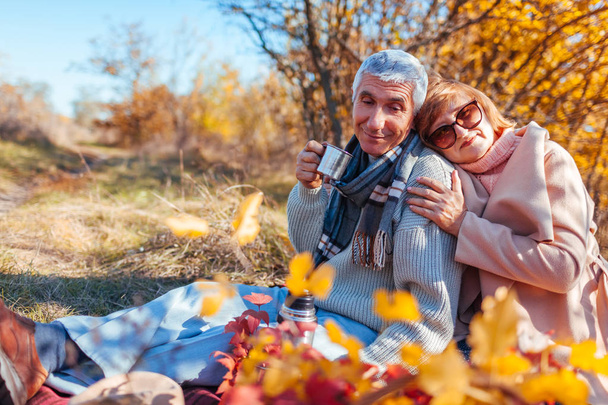 Starší pár s čajem v podzimním lese. Šťastný muž a žena užívat piknik a přírodou. Usmívající se muž vylévající čaj z termosky - Fotografie, Obrázek