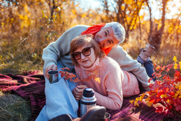 Старшая пара пьет чай в осеннем лесу. Счастливые мужчина и женщина наслаждаются пикником и природой. Улыбающийся человек, наливающий чай из термоса
 - Фото, изображение