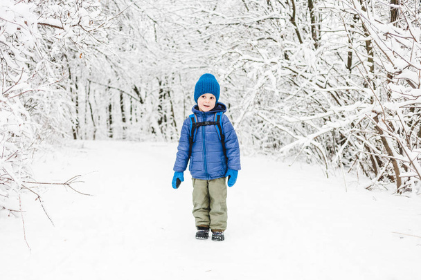 Un niño con una mochila camina a lo largo del sendero de nieve. Un niño camina en el bosque en invierno. Un niño pasa tiempo en la naturaleza
. - Foto, imagen