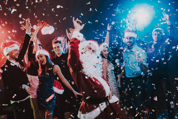 Man in Santa Claus Costume on New Year Party. Happy New Year. People Have Fun. Indoor Party. Celebrating of New Year. Young Women in Dresses. Young Men in Suits. Happy People. Man with White Beard. - Foto, Bild
